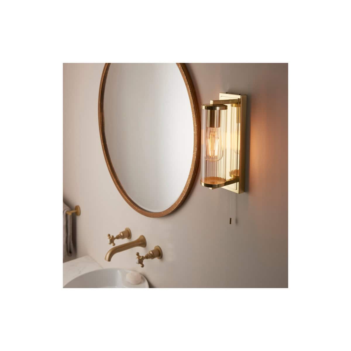 Sleek modern bathroom wall sconce with amber glass shade, mounted beside a large oval wooden-framed mirror, featuring traditional gold-tone fixtures and soft lighting for elegant bathroom decor.