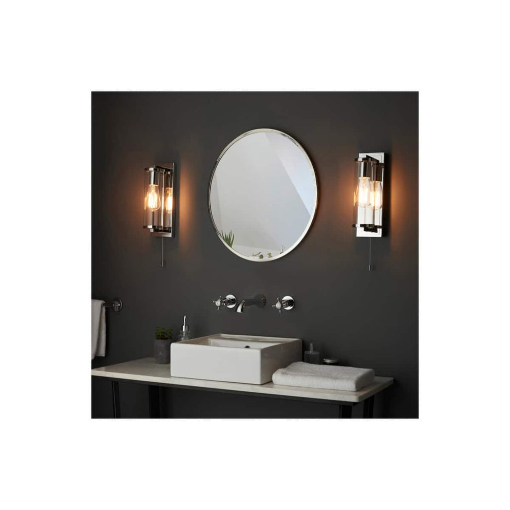 Sleek modern bathroom vanity with black wall, round mirror, and stylish wall sconces providing warm lighting, perfect for contemporary bathroom designs.