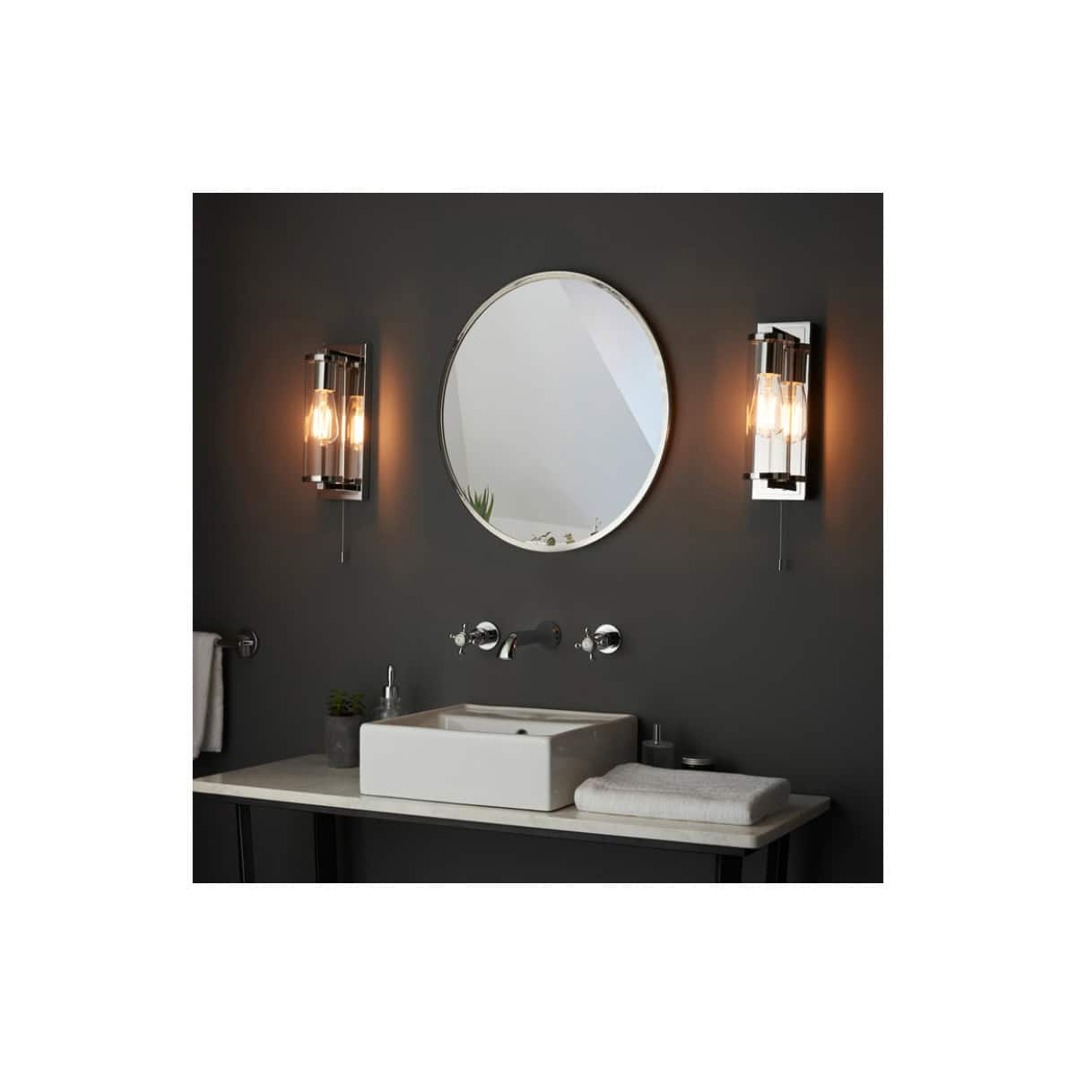 Sleek modern bathroom vanity with black wall, round mirror, and stylish wall sconces providing warm lighting, perfect for contemporary bathroom designs.