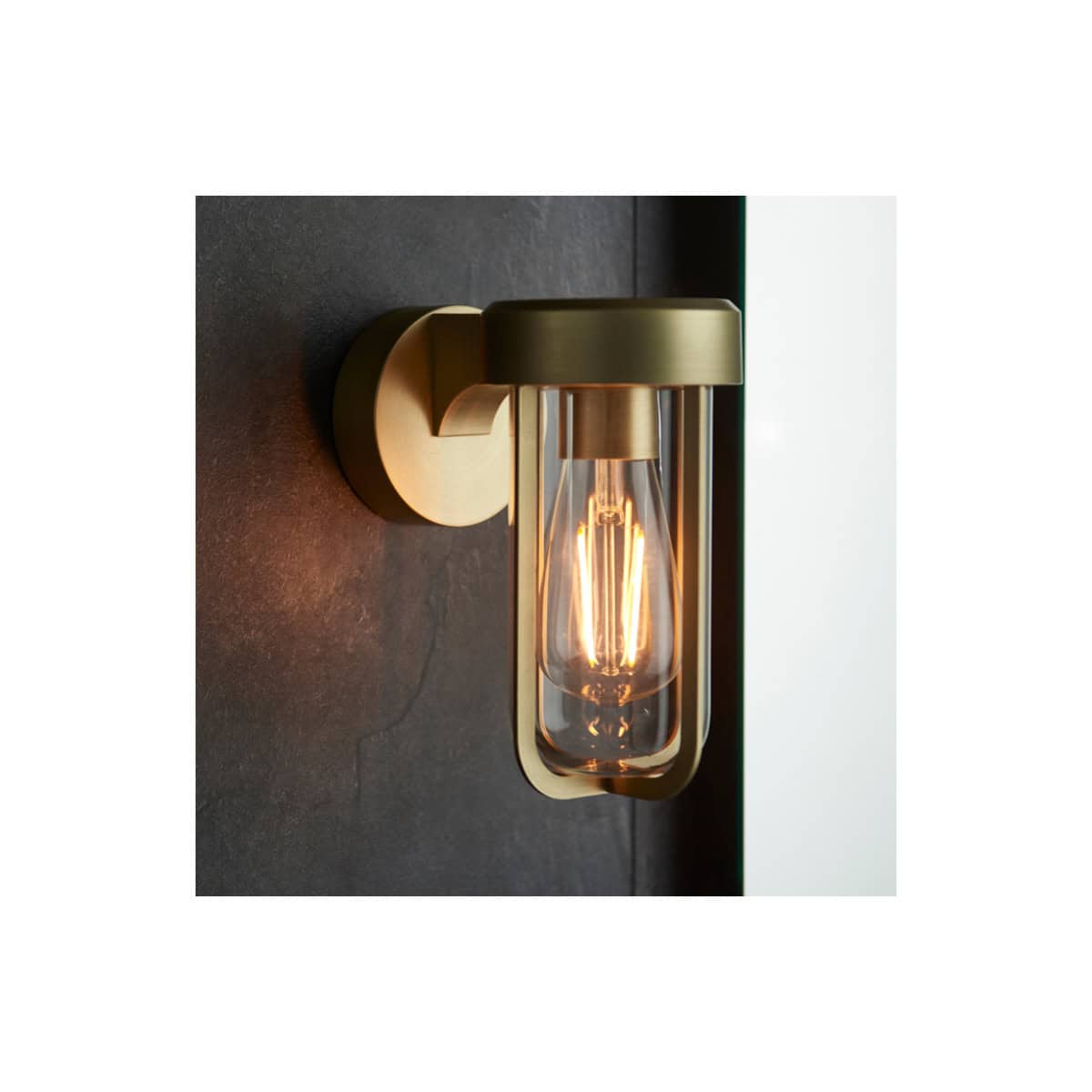 Modern brass wall-mounted bathroom light with clear glass shade and vintage filament bulb for stylish illumination.