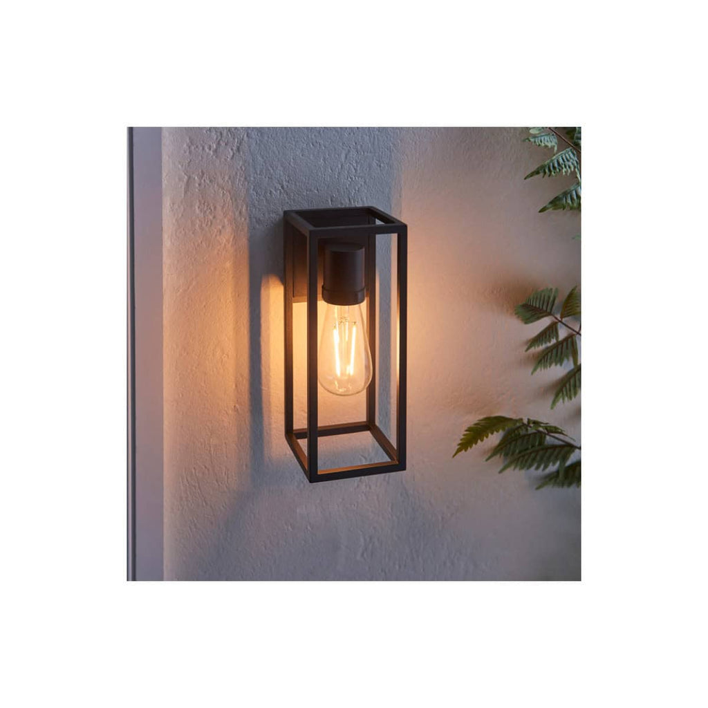 Modern black metal wall-mounted bathroom light fixture with an exposed filament bulb on textured white wall, ideal for contemporary bathroom lighting.