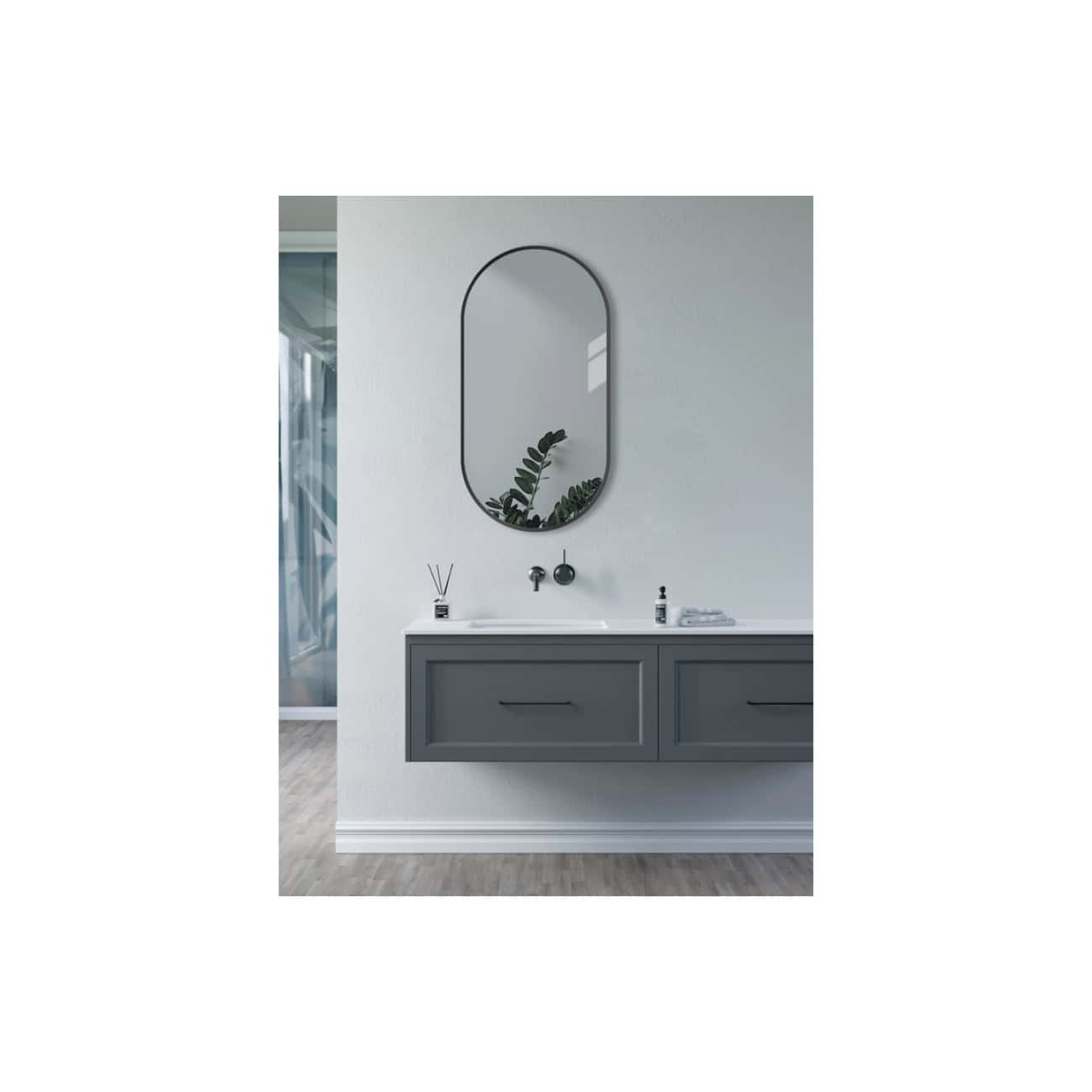 Modern bathroom vanity with a sleek grey cabinet, white countertop, black wall-mounted faucet, and an oval mirror with a black frame, complemented by minimalist decor and greenery.