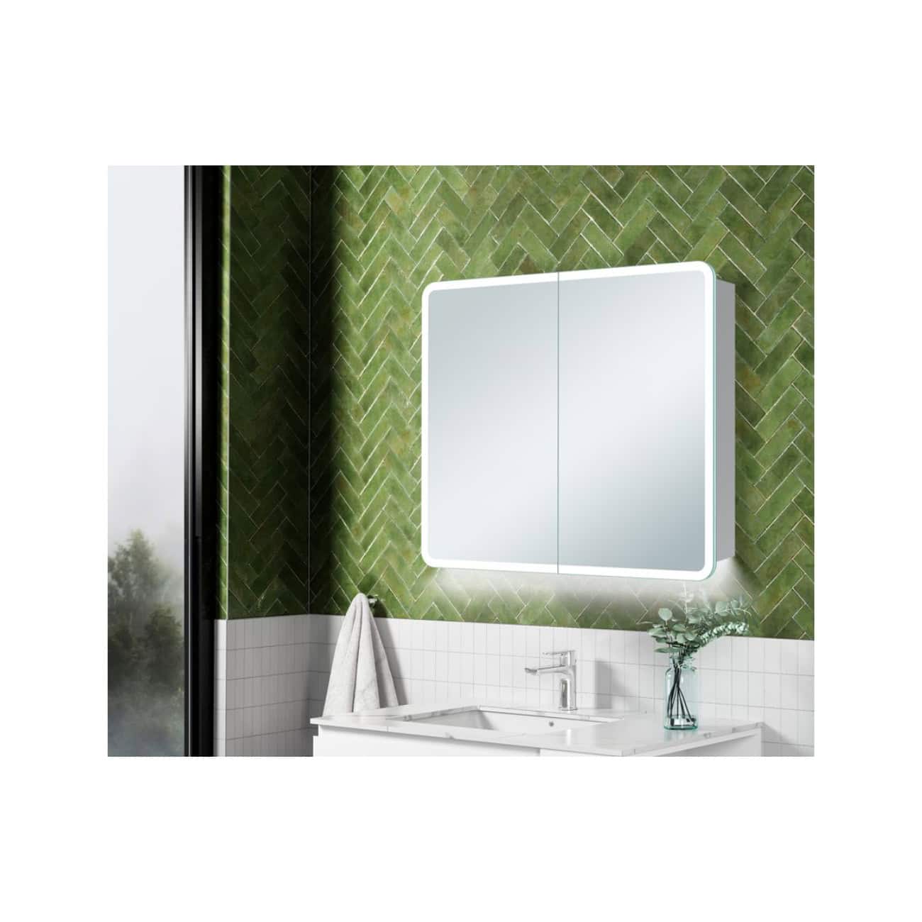 Light-up LED bathroom mirror with built-in lighting above a white sink and green tiled wall. Modern bathroom vanity with a clean, minimalist design ideal for contemporary bathroom renovations.
