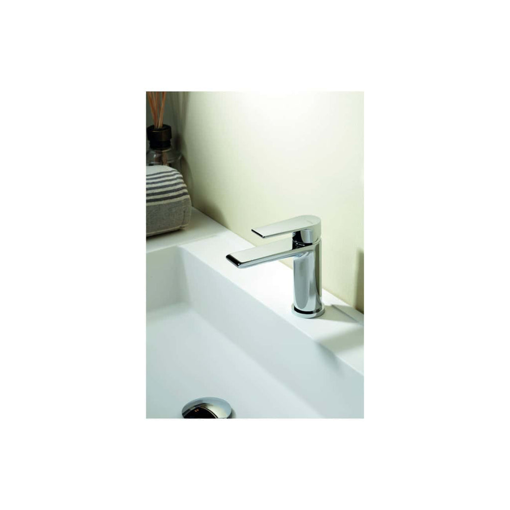 Polished chrome bathroom tap on white ceramic sink with a spoon rest and decorative items in the background, showcasing modern bathroom fixtures and sleek design.