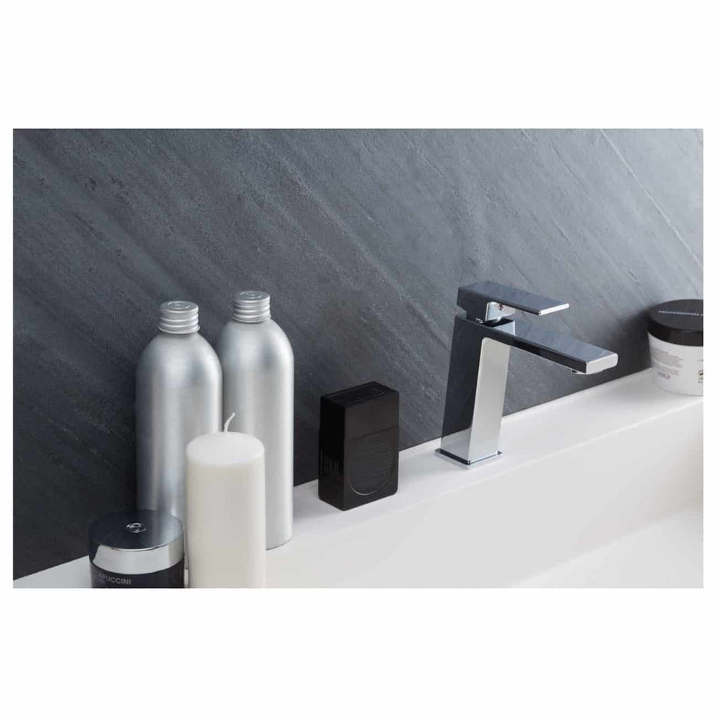 Sleek modern bathroom sink area with minimalist silver and black accessories, including bottles, a soap dispenser, and a contemporary faucet against a textured dark grey wall.