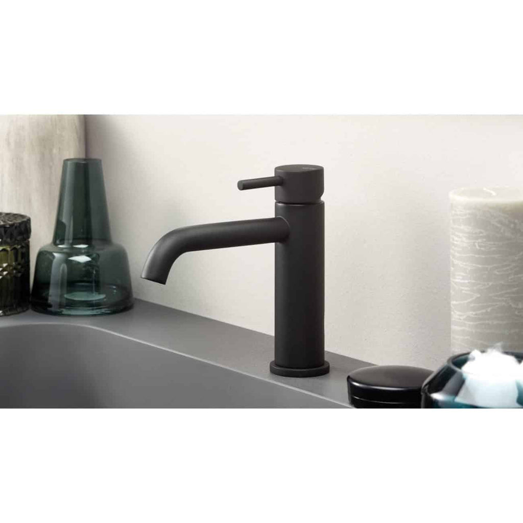 Black matte bathroom mixer tap on a grey countertop with decorative vases and a tissue roll, showcasing modern bathroom installation and design.