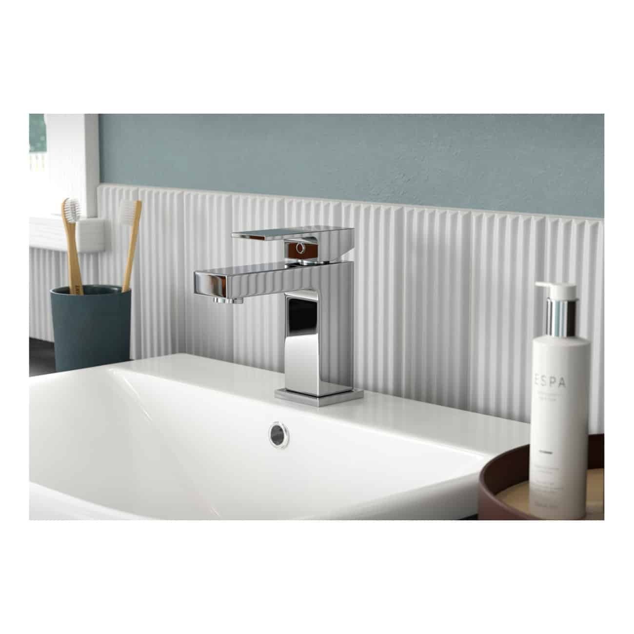 Sleek modern bathroom sink with chrome faucet, set against a textured white tile wall, complemented by bathroom accessories and personal care products for a contemporary bathroom look.