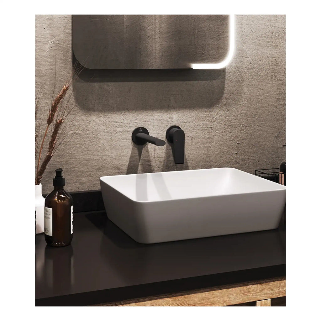 Sleek square white bathroom sink with matte black wall-mounted faucet and modern mirror with LED lighting, featuring a minimalist design for contemporary bathroom decor.