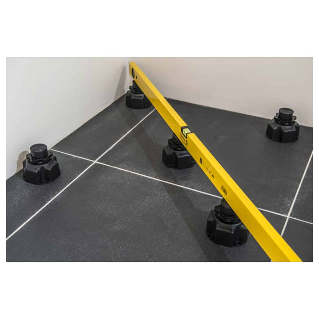 Leveling a tiled bathroom floor with a yellow spirit level and adjustable levelling feet for precise alignment.