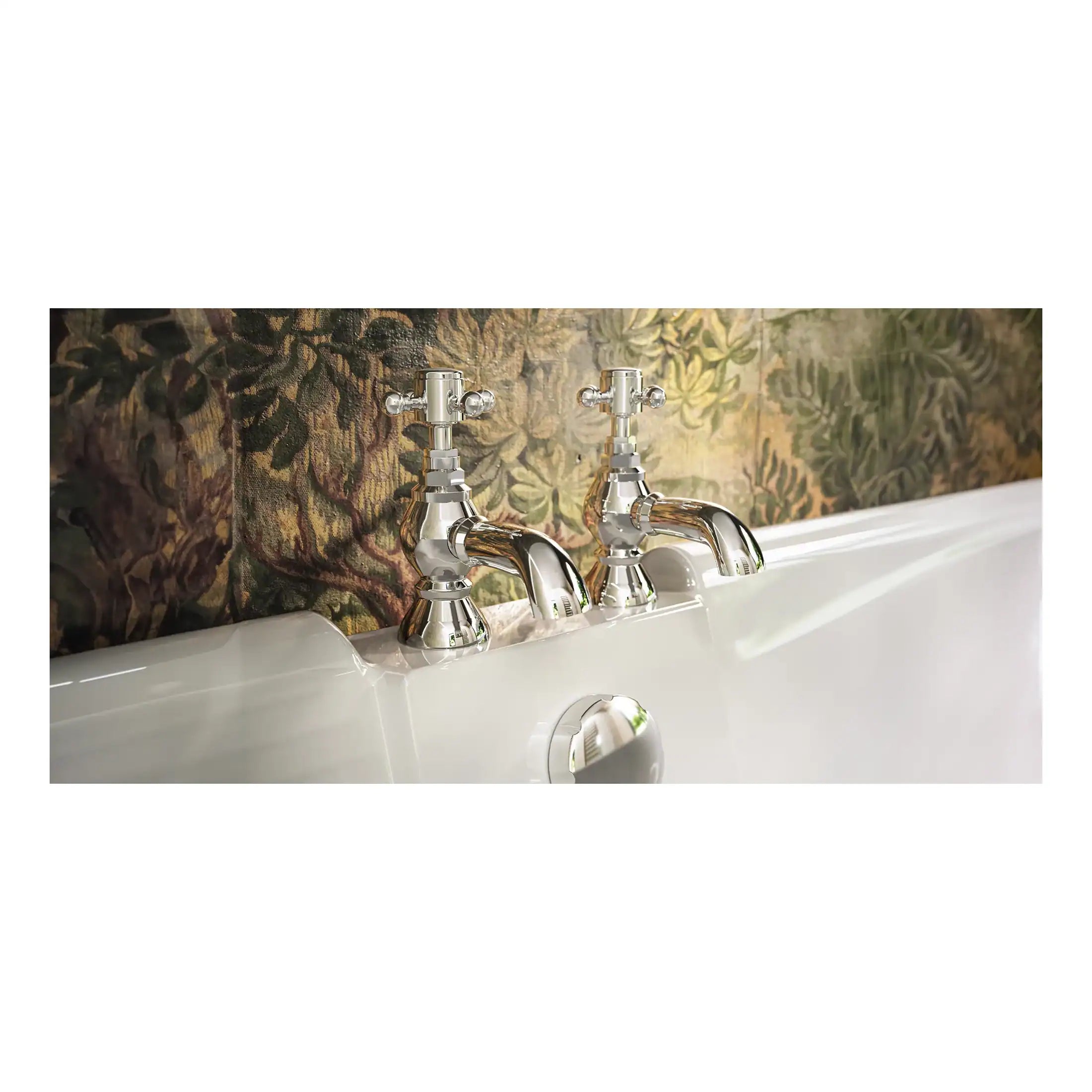 Brass bathroom taps with traditional cross handles mounted on a white bathtub against a decorative floral wallpaper backdrop. Suitable for classic and vintage bathroom designs, combining elegance with functionality.