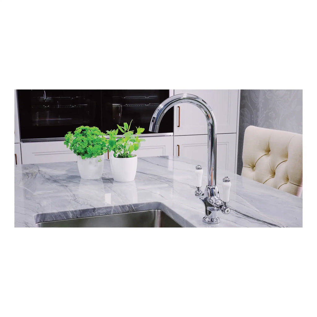 Polished chrome kitchen tap with a high-arc spout on a modern marble worktop, complemented by potted herbs, in a contemporary kitchen setting.