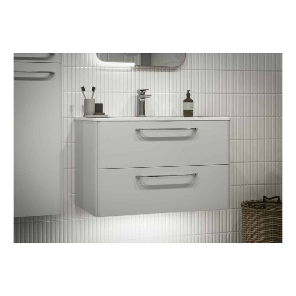 Sleek white bathroom vanity with two drawers, minimalist design, and modern chrome handles, set against a white tiled wall, with bathroom accessories and a woven basket nearby.