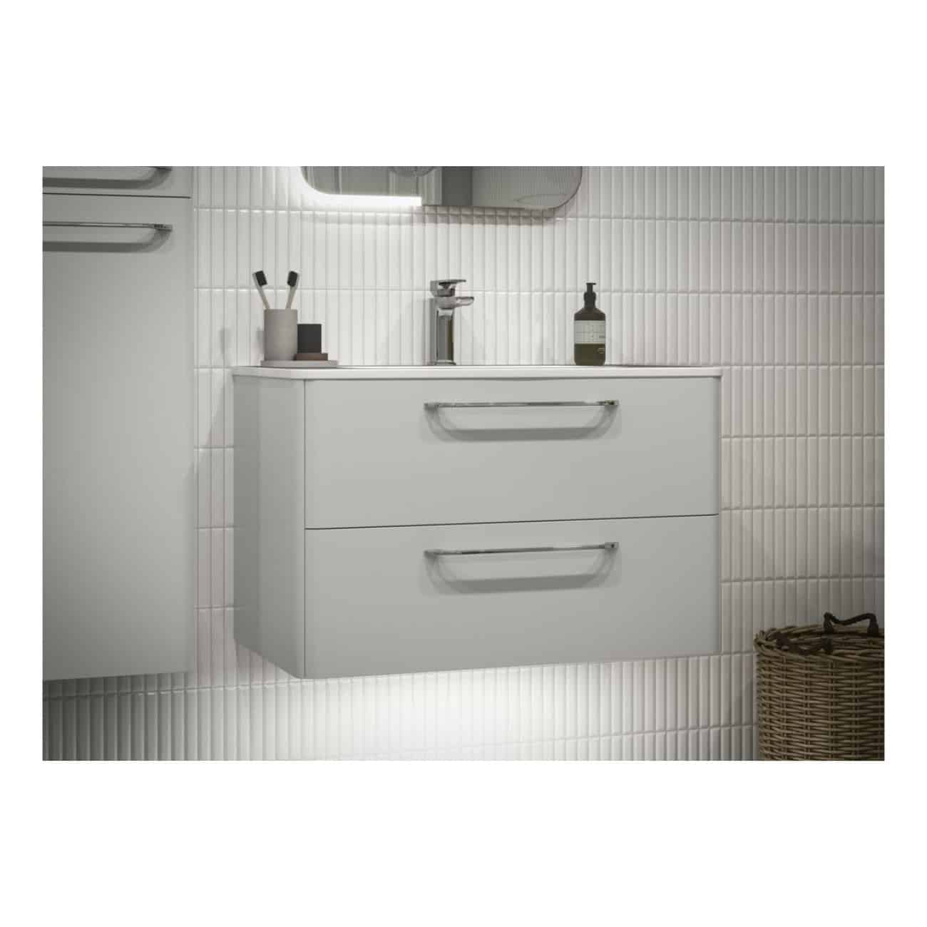 Sleek white bathroom vanity with two drawers, minimalist design, and modern chrome handles, set against a white tiled wall, with bathroom accessories and a woven basket nearby.