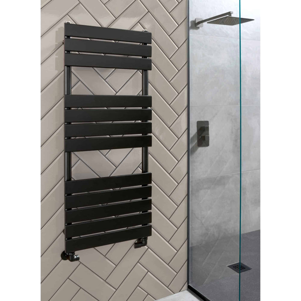 Radiator-style towel warmer in black mounted on beige tiled wall in modern bathroom.