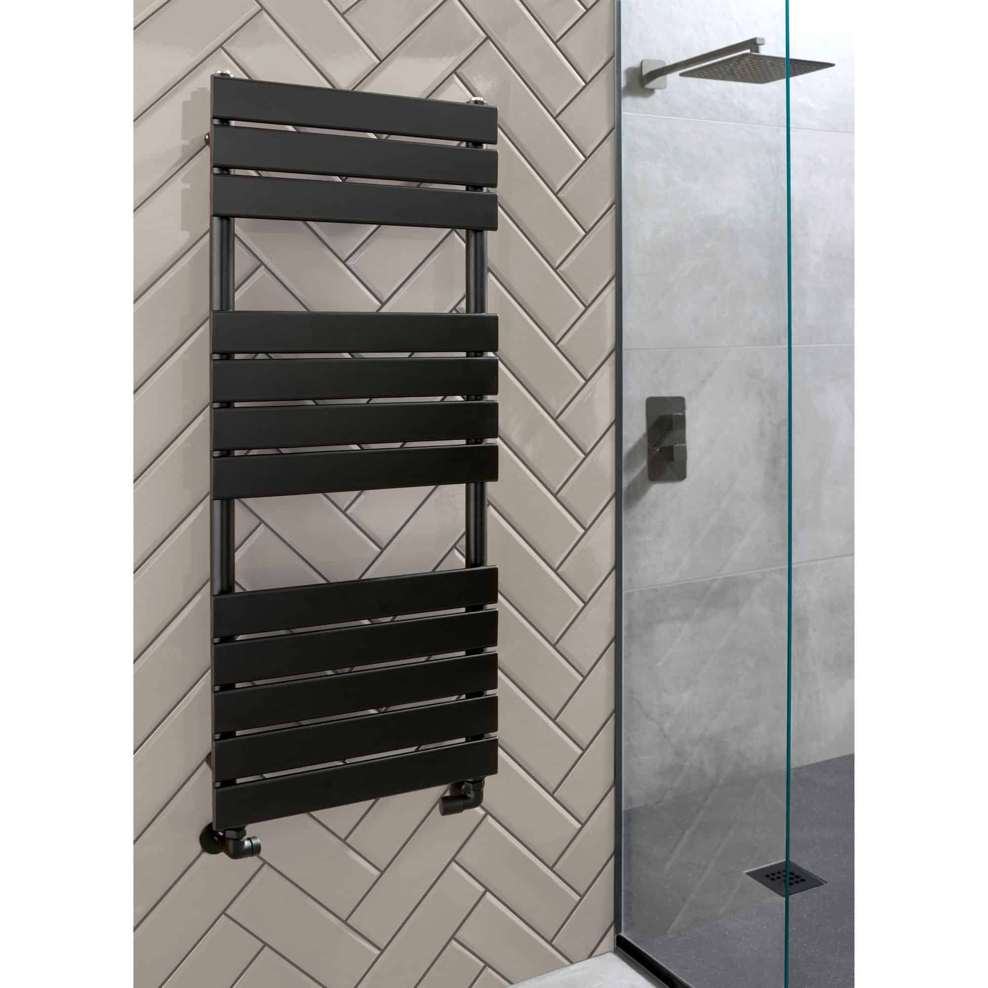 Radiator-style towel warmer in black mounted on beige tiled wall in modern bathroom.
