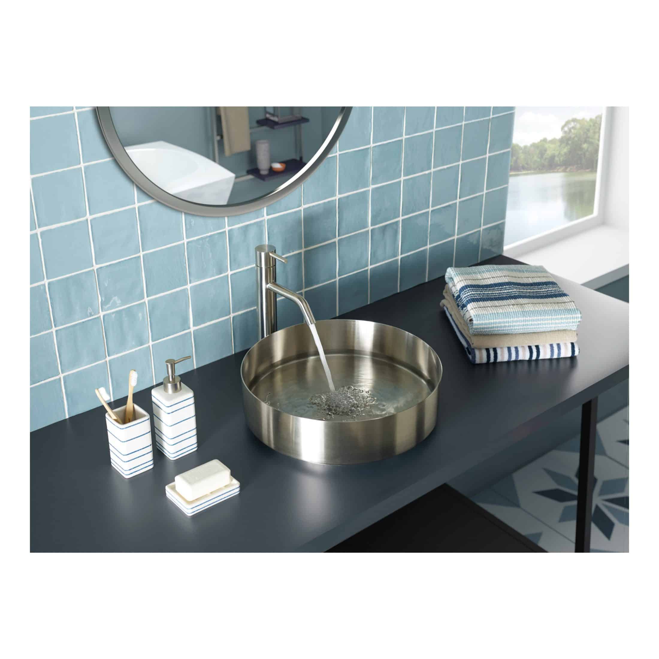 Brushed stainless steel bathroom sink with water running, modern black countertop, neatly folded blue and white towels, minimalist bathroom accessories, blue tiled wall, scenic window view in bathroom, stylish bathroom design, contemporary bathroom with elegant fixtures.