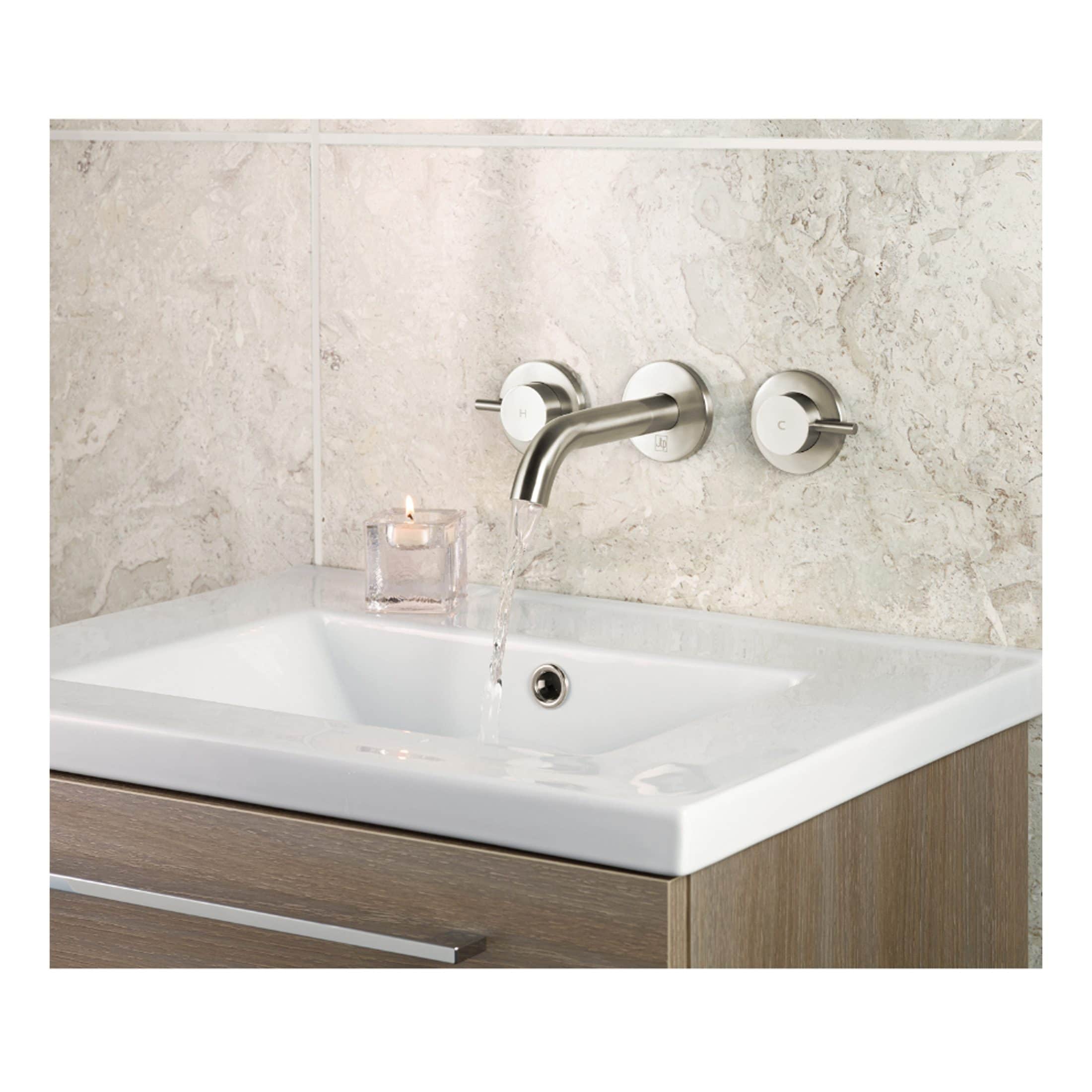 Sleek modern bathroom sink with stainless steel tap, wall-mounted controls, beige marble tiles, and a lit candle in a glass holder for a calming bathroom ambiance.