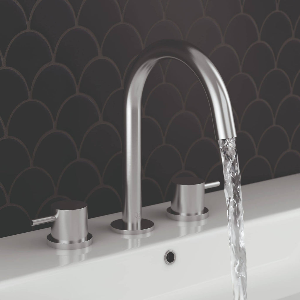Shiny stainless steel kitchen tap with water flowing over a white basin, set against a dark decorative tile backsplash.