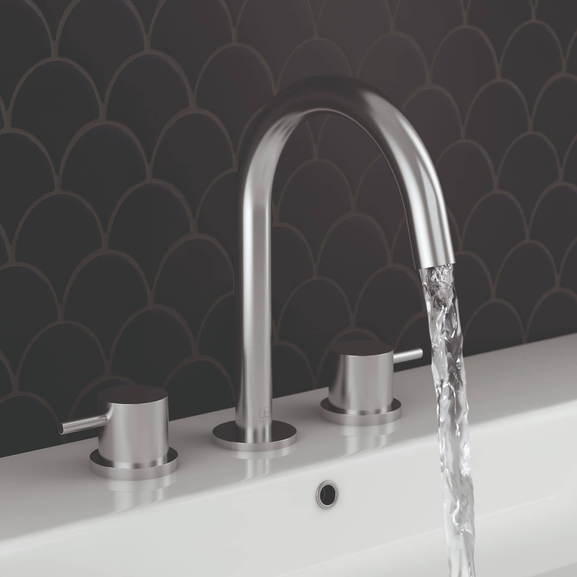 Shiny stainless steel kitchen tap with water flowing over a white basin, set against a dark decorative tile backsplash.