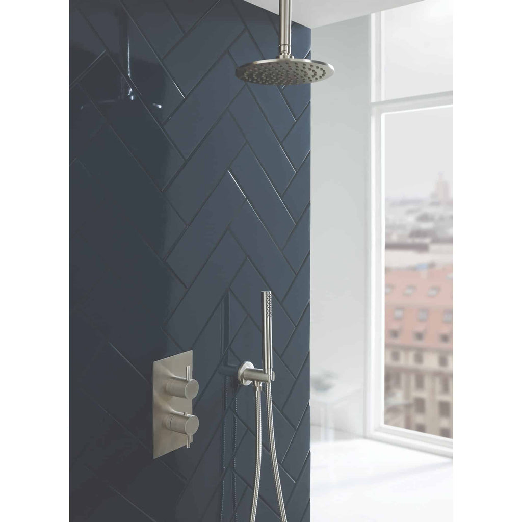 Sleek modern shower area with dark navy herringbone tiles, stainless steel showerhead, and handheld shower attachment, bright natural light from large window interior design bathroom inspiration.