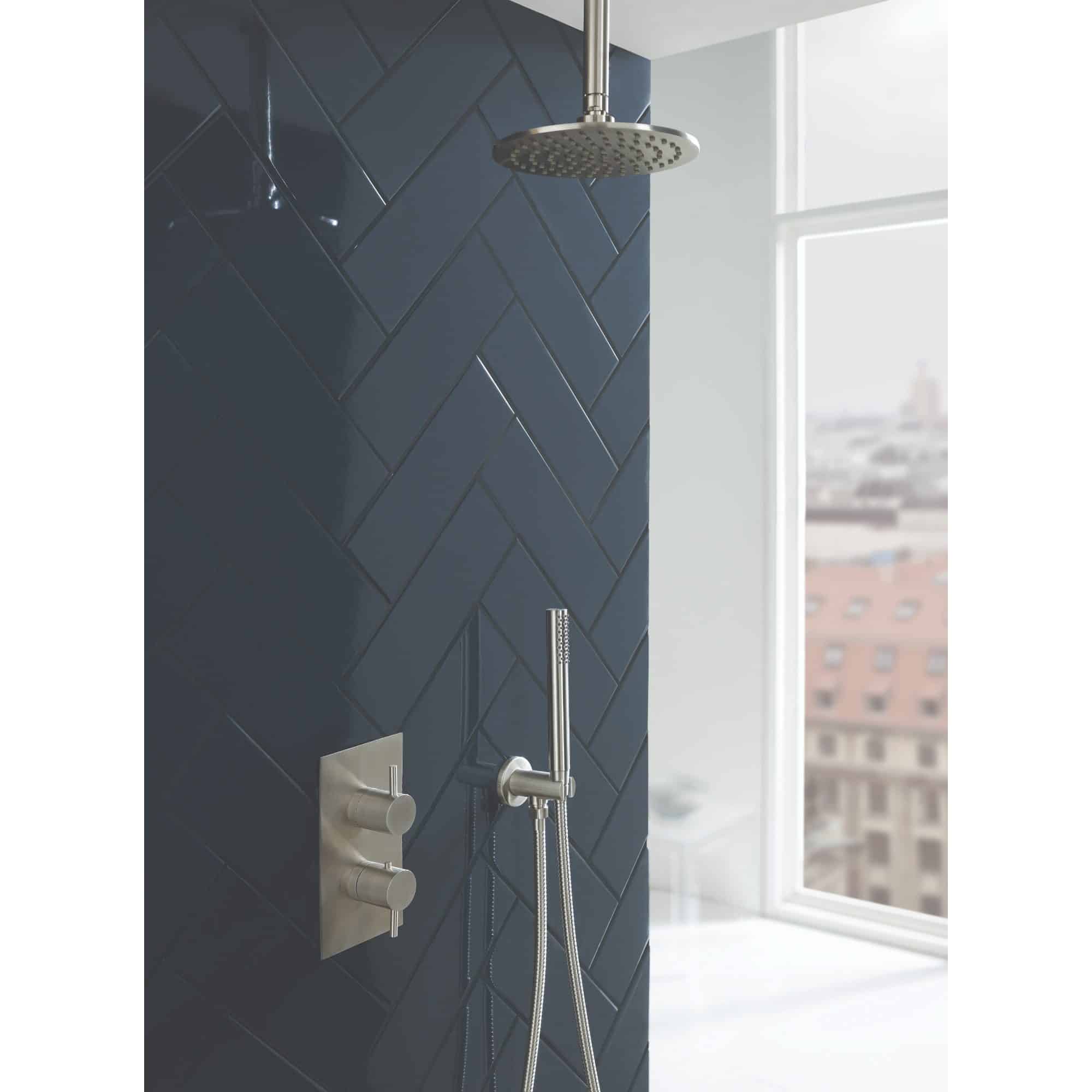 Sleek modern shower area with dark navy herringbone tiles, stainless steel showerhead, and handheld shower attachment, bright natural light from large window interior design bathroom inspiration.
