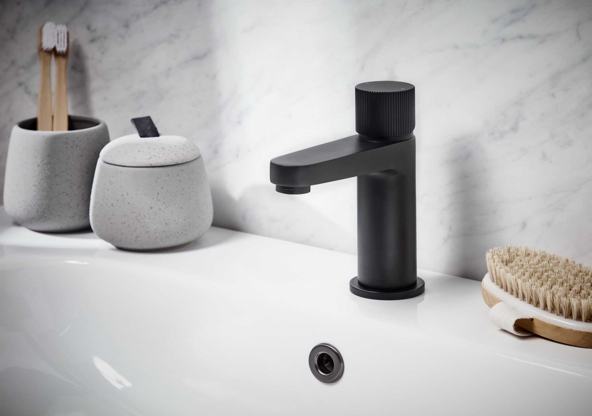 Sleek black bathroom tap with modern matte finish, situated on a clean white sink with bathroom accessories like toothbrush holders and scrub brush for stylish bathroom design.