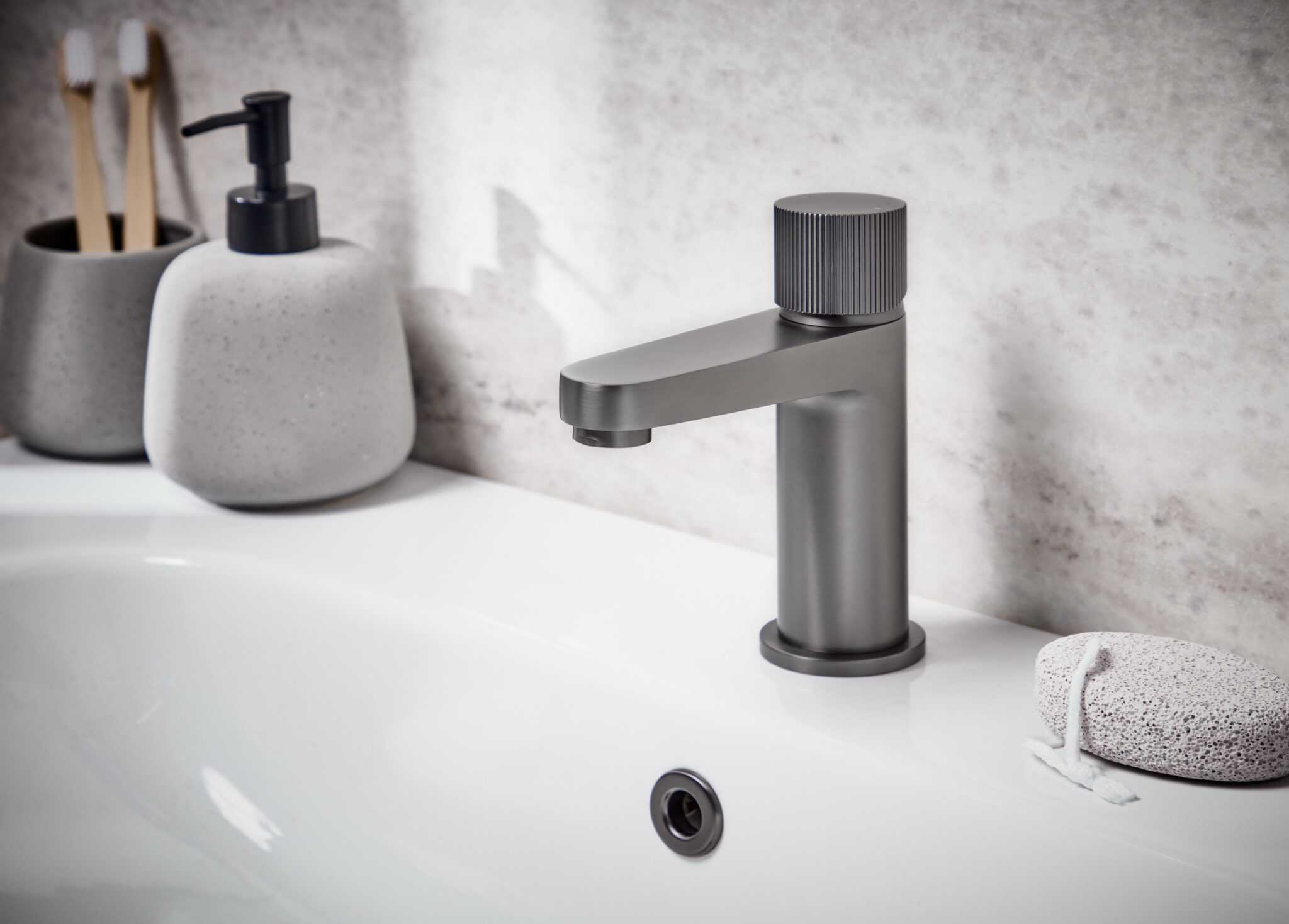 Modern matte grey bathroom tap beside soap dispensers and pumice stone, ideal for minimalist bathroom renovations and kitchen upgrades.