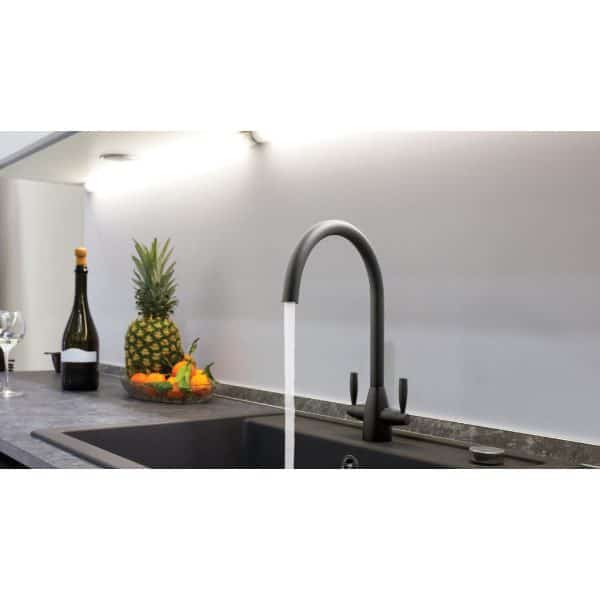 Sleek black kitchen tap with water flowing over modern grey granite countertop in contemporary bathroom setting. Fruit and wine bottle decor add a stylish touch.