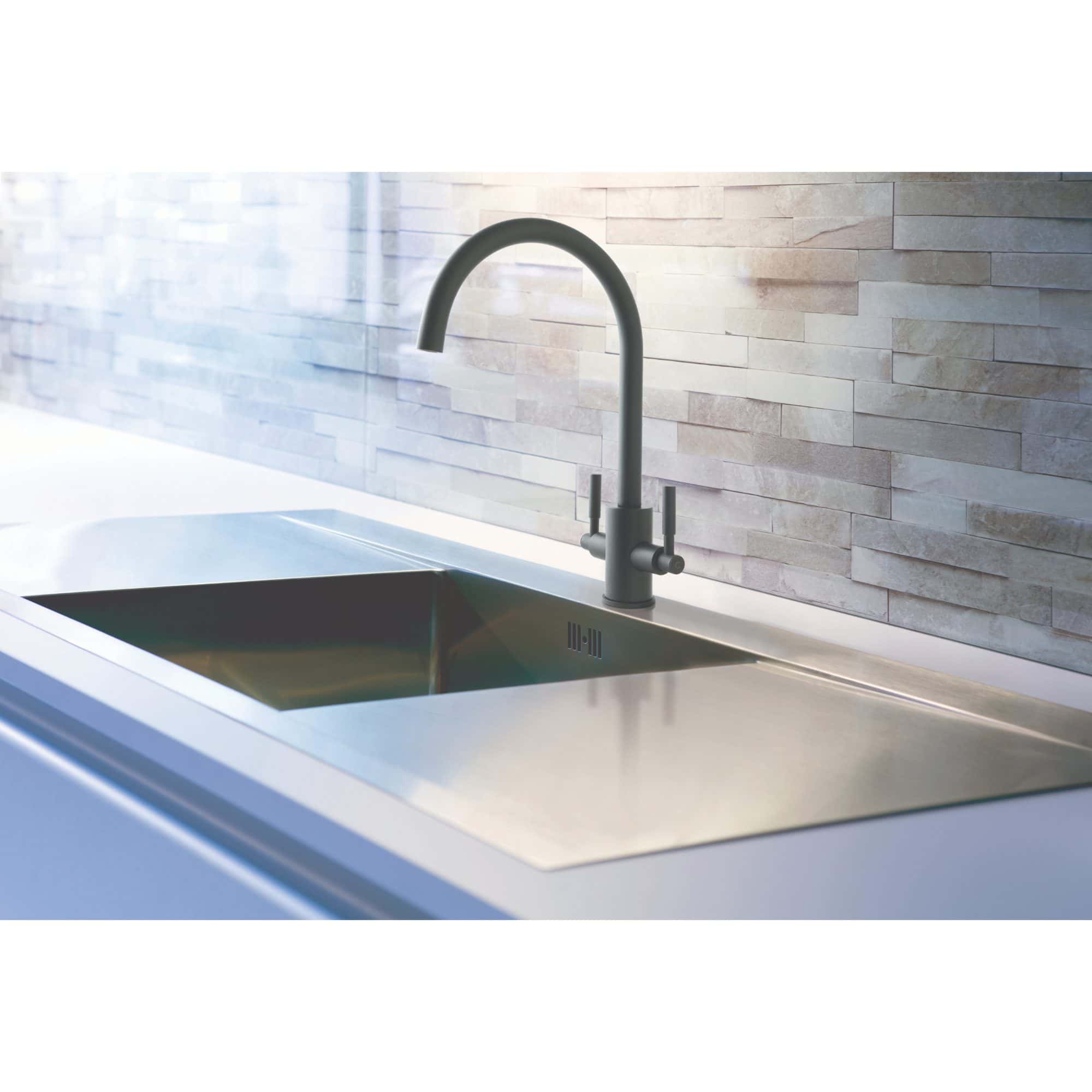 Sleek modern kitchen sink with stainless steel finish and black faucet, set against a textured light stone wall, perfect for contemporary bathroom or kitchen renovations.