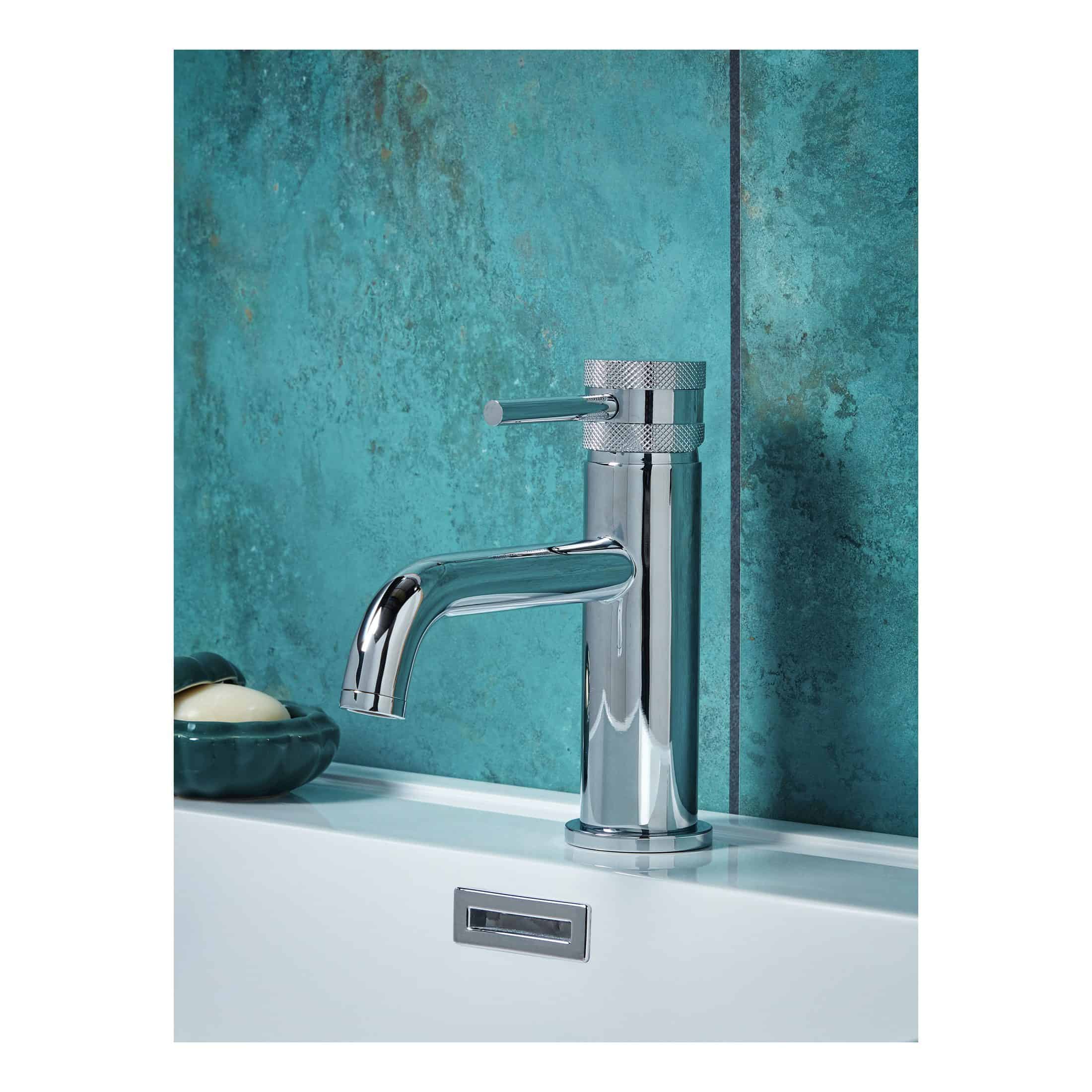 Polished chrome bathroom tap with modern design, installed on a white countertop with a textured teal bathroom wall in the background.
