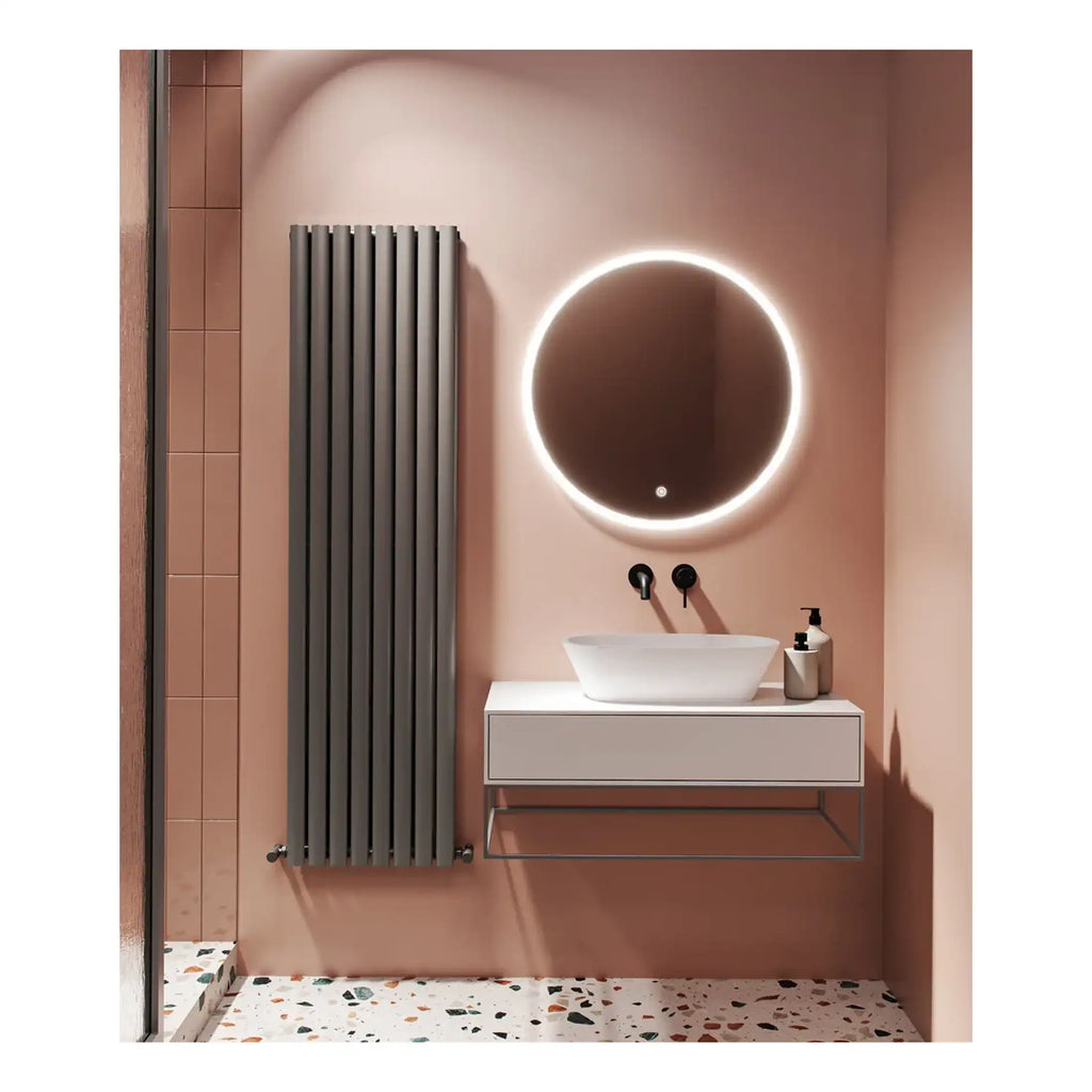 Modern bathroom with illuminated round mirror, vessel sink, black wall-mounted faucet, and sleek vanity unit in a soft pink wall setting, featuring a tall vertical radiator and terrazzo flooring.