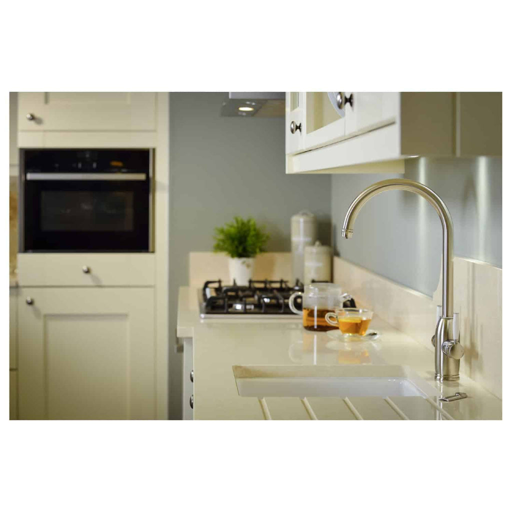 A modern kitchen with cream cabinetry, stainless steel fixtures, and a built-in oven, featuring a beige countertop with a sink, a chrome faucet, and a stove with tea and coffee cups nearby.