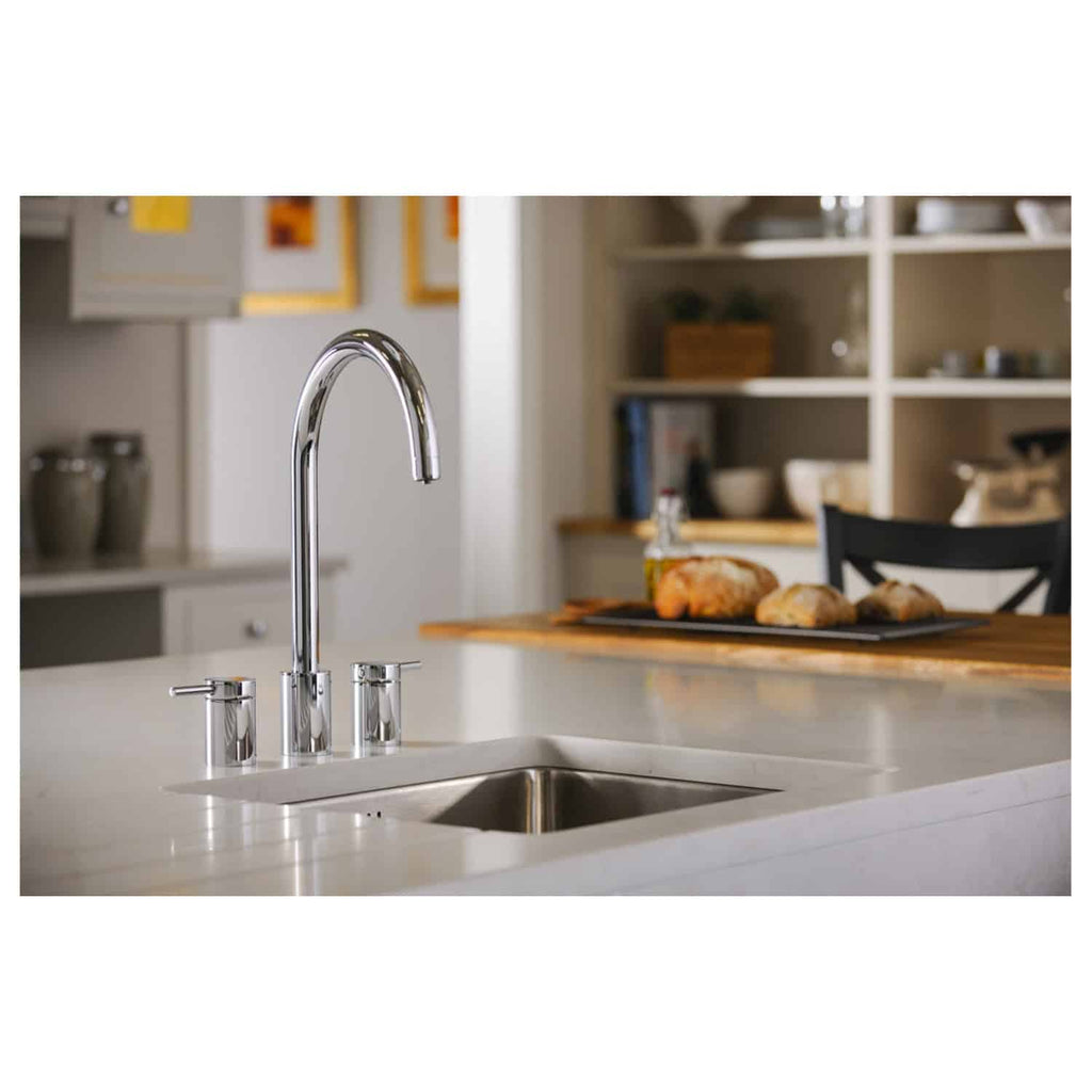 Sleek chrome kitchen sink with modern tap and soap dispensers in a contemporary kitchen setting, featuring an open shelving unit and baking bread on a wooden table, highlighting stylish and functional bathroom and kitchen fixtures.