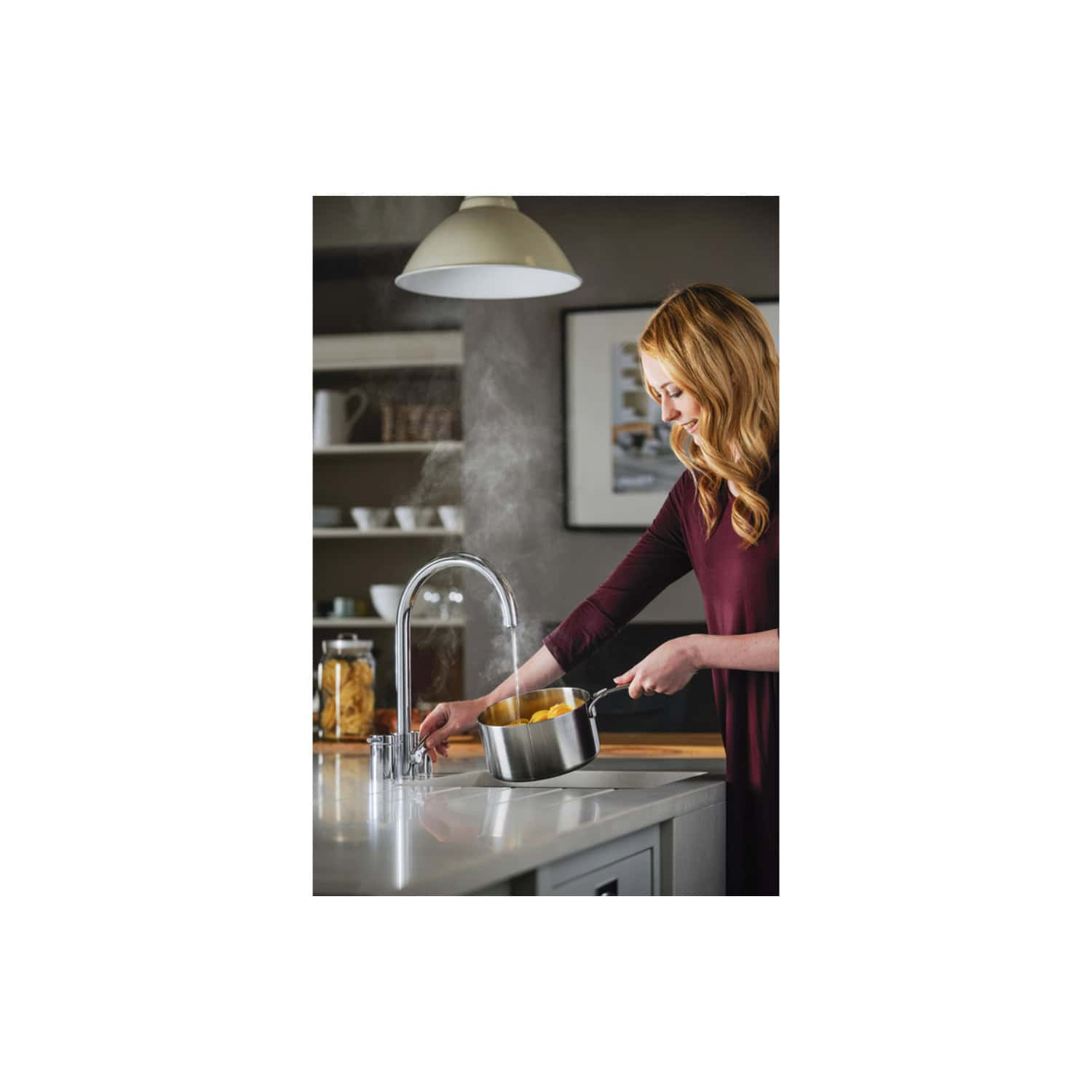 Shiny kitchen sink with a modern tap, steam rising from boiling food, woman preparing a meal in a contemporary kitchen setting, bright lighting, and organised shelves in the background.