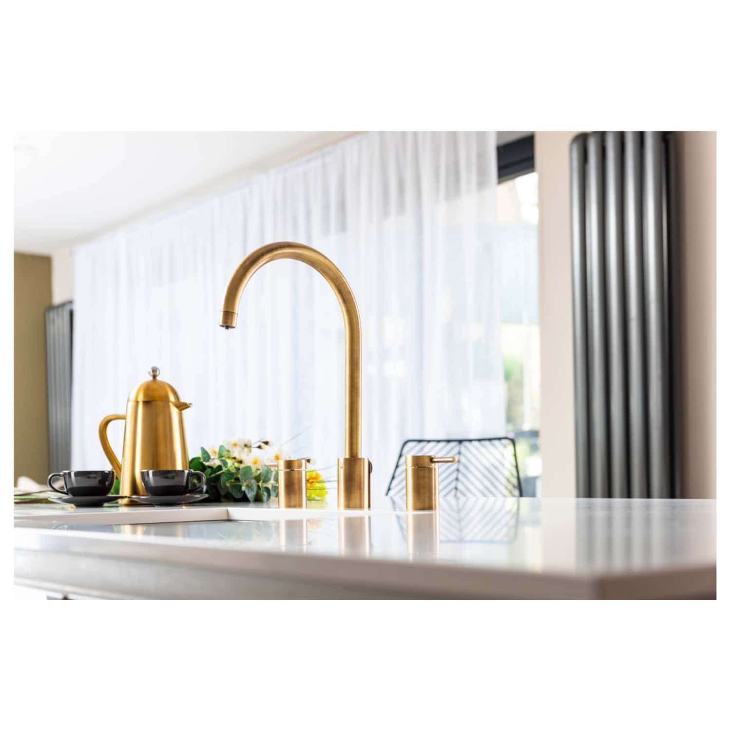 Shiny gold kitchen sink faucet with matching soap dispenser and black teapot, accompanied by fresh flowers on a white kitchen countertop, highlighting luxury bathroom fixtures and modern kitchen design.