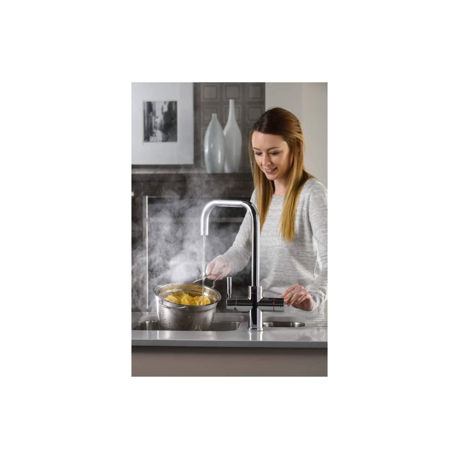 Steamy kitchen with modern chrome faucet, woman cooking pasta under hot running water in a sleek home environment, showcasing contemporary bathroom and kitchen fixtures.