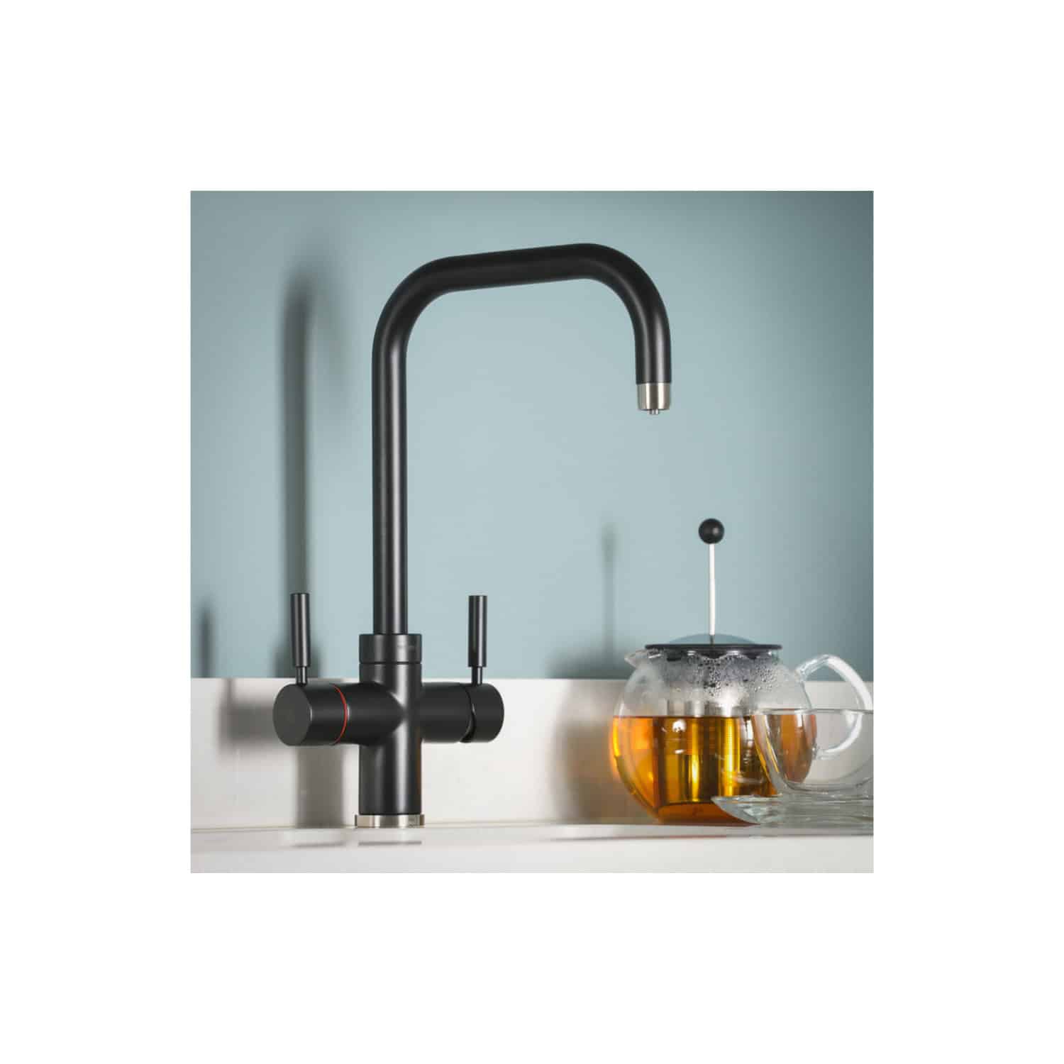 Black modern kitchen tap with a curved spout and two lever handles, paired with a glass teapot filled with tea on a white kitchen countertop.