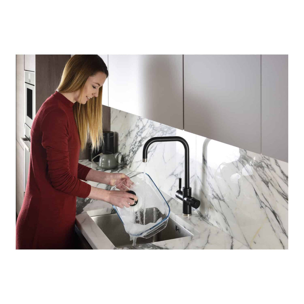 A woman washing a glass food storage container at a modern kitchen sink with marble countertops and grey cabinetry, demonstrating stylish and functional kitchen design.