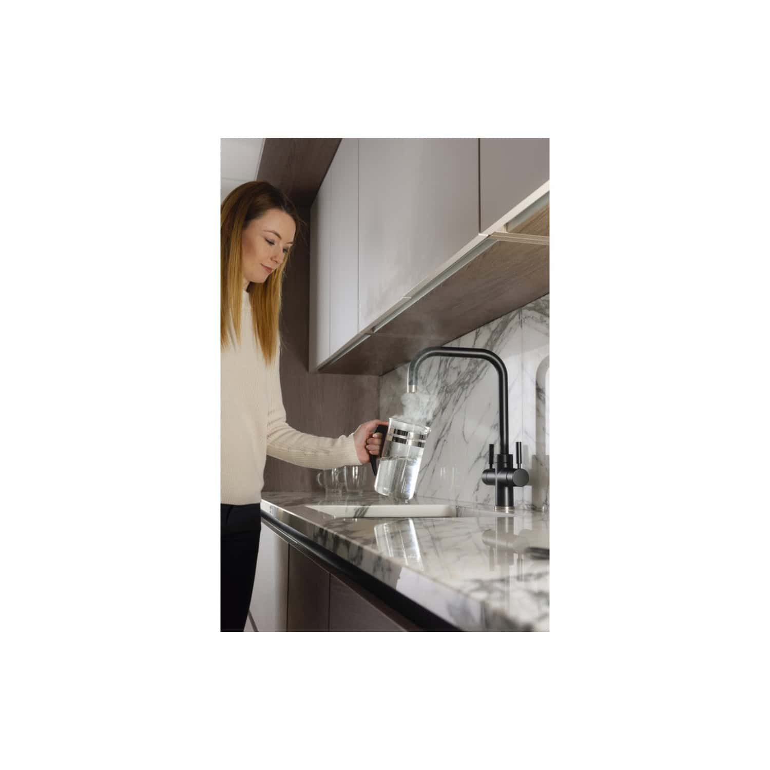 Modern kitchen with innovative bubly water filter attached to black matte tap, woman filling glass with sparkling water, sleek white marble countertop and contemporary cabinetry, promoting healthier drinking habits.