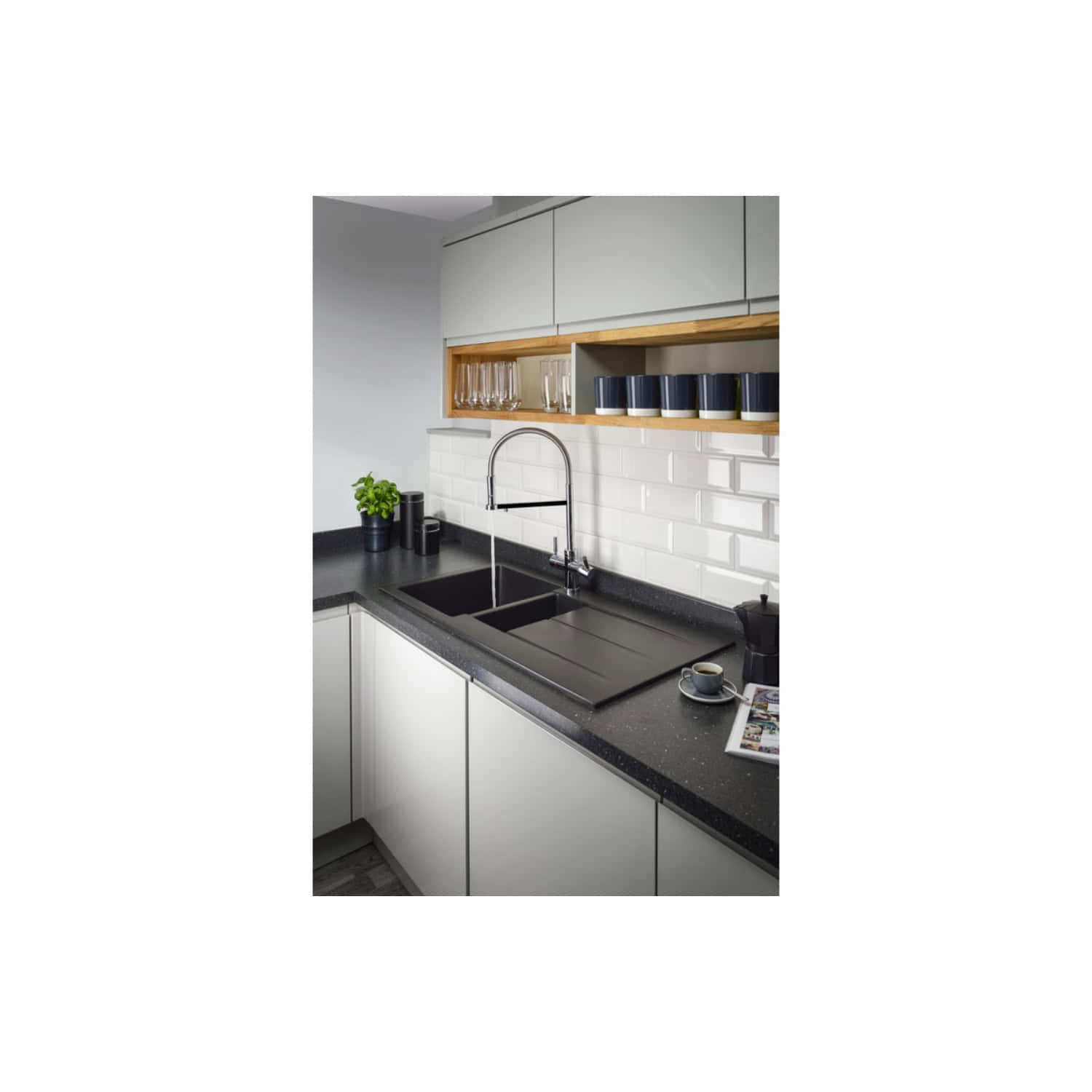Sleek modern kitchen with black countertop, white cabinetry, glass and black canisters, kitchen sink, open wooden shelves, white subway tile backsplash, coffee cup, coffee maker, and potted plant.