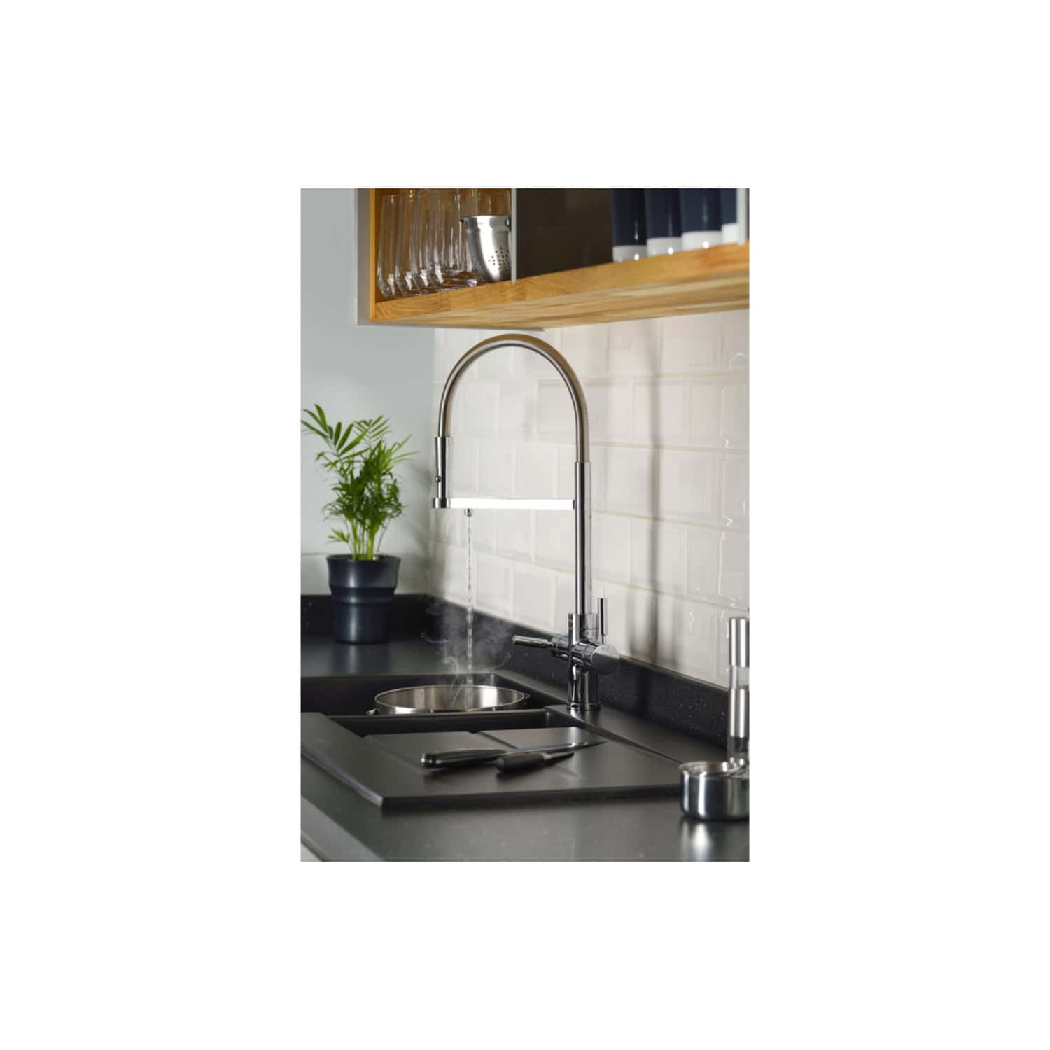 Sleek kitchen sink with chrome faucet, black countertop, white backsplash tiles, wooden shelves, and a small potted plant for modern bathroom or kitchen design.