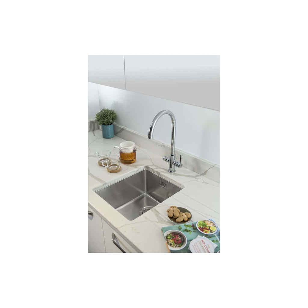 Wideshot of a modern kitchen sink with a sleek chrome faucet, set in a white marble countertop, with tea and biscuits, a potted plant, and a minimalistic backsplash, showcasing elegant bathroom and kitchen design.