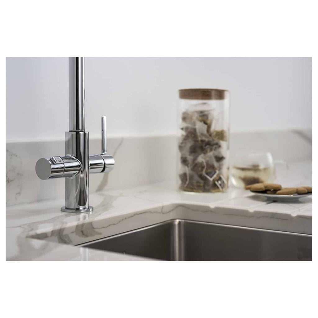 Sleek chrome kitchen tap installed on a white marble countertop with a stainless steel sink, surrounded by a jar of seashells and a plate of biscuits, highlighting modern bathroom and kitchen fixtures.