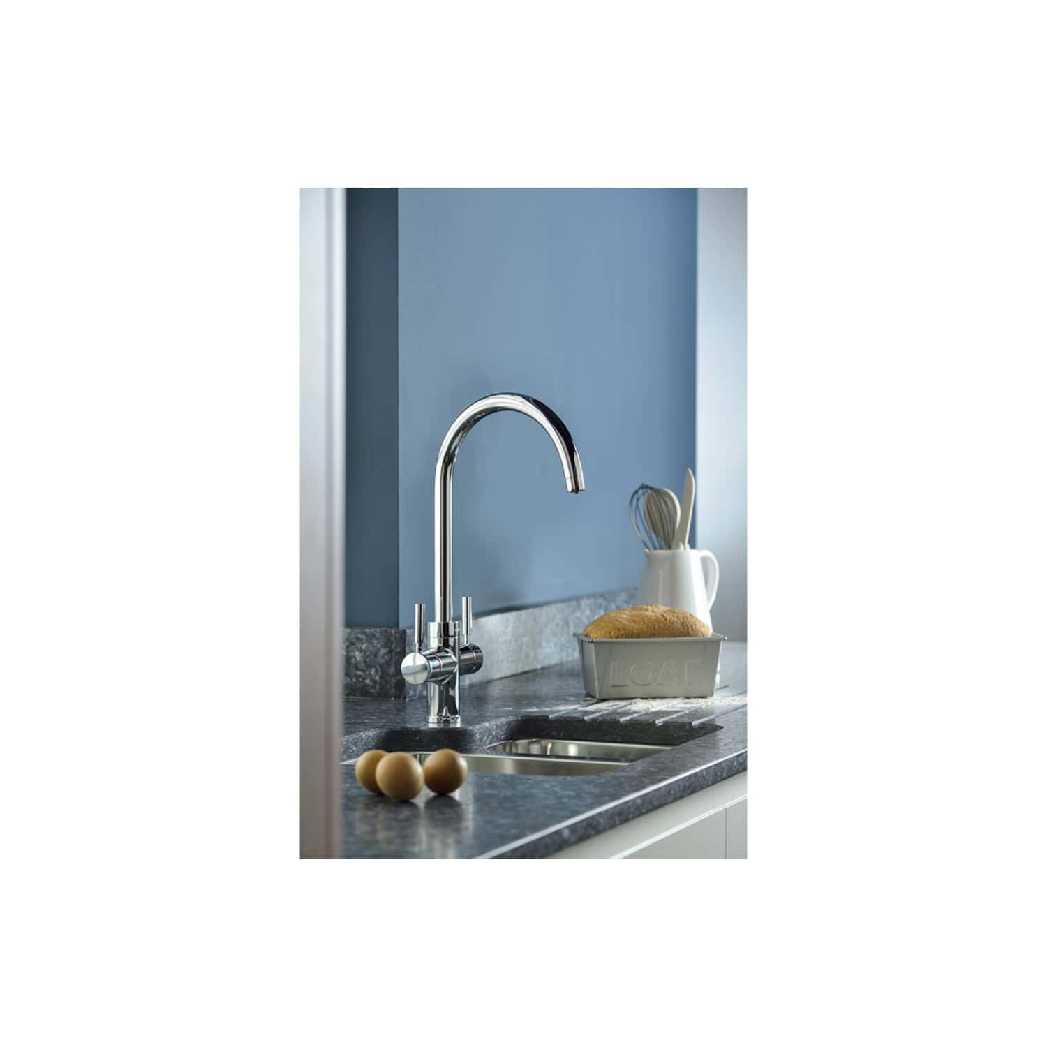 Shiny chrome kitchen tap with grey stone worktop and blue wall background, stylish bathroom sink area with soap and eggs.