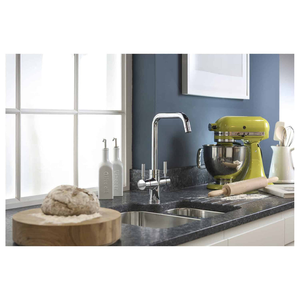 Shiny chrome kitchen tap with black granite work surface, yellow stand mixer, white ceramic bottles, dough on wooden board, and window with white frame, modern kitchen design with stylish accessories.