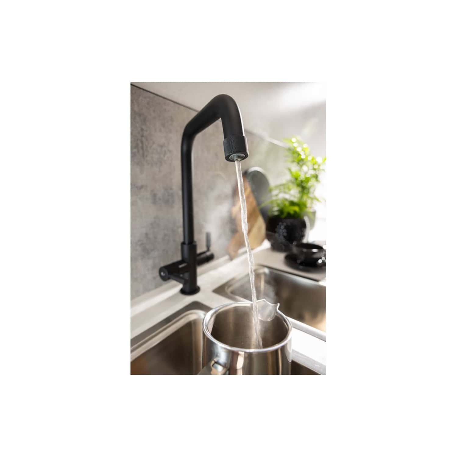 Sleek black kitchen tap with water pouring into a stainless steel kettle, modern sink setup, and decorative green plant in the background, highlighting contemporary bathroom and kitchen fixtures.