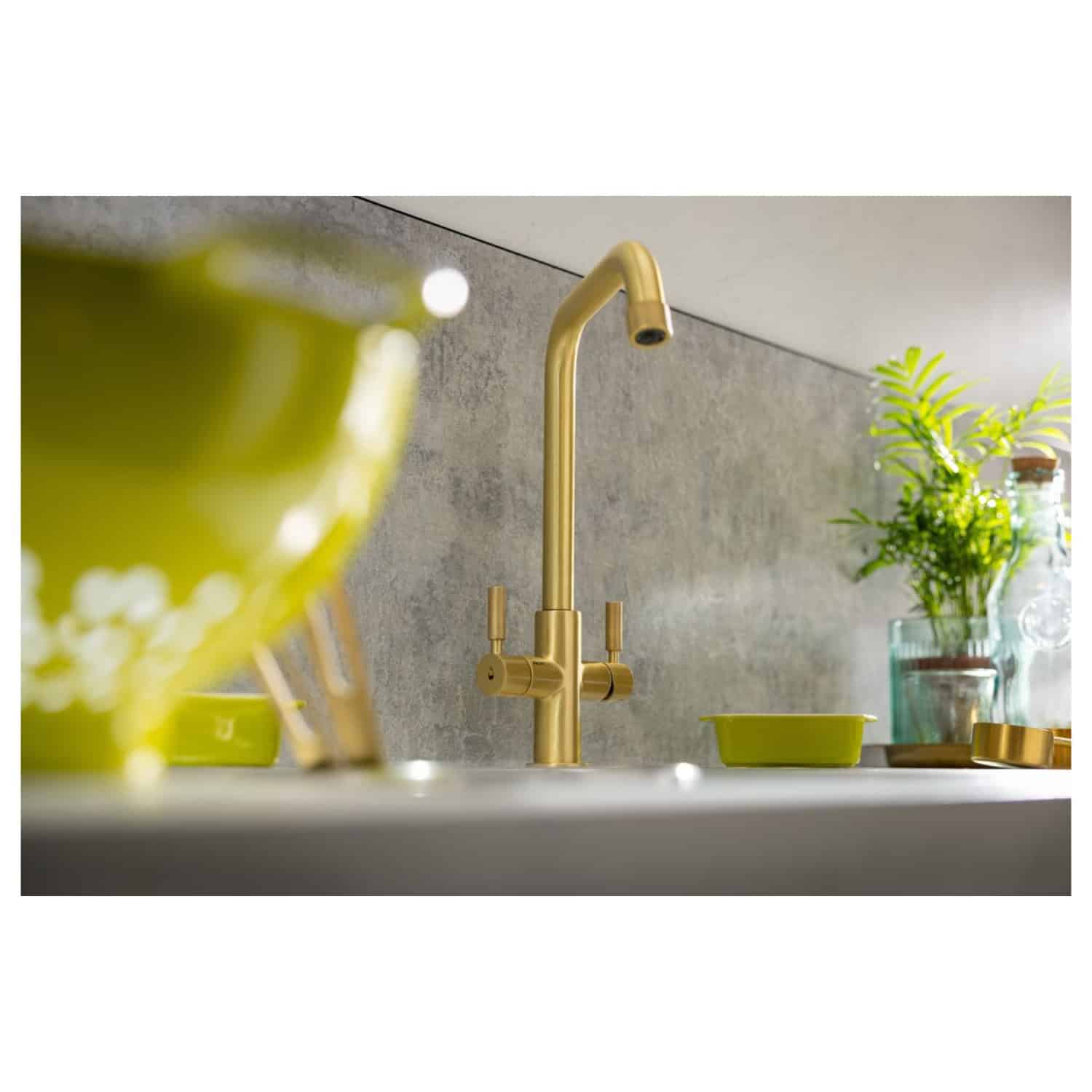 Sleek gold kitchen tap with a modern design, complemented by vibrant green dishware and fresh plants for a stylish and contemporary bathroom or kitchen setting. Perfect for upgrading your space.