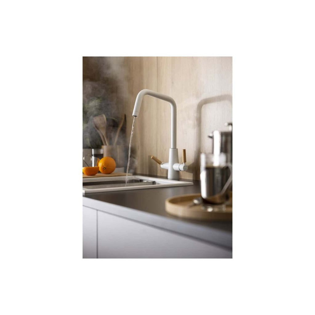 A sleek white kitchen faucet with a modern design, installed over a stainless steel sink, with fresh oranges and kitchen utensils in the background.