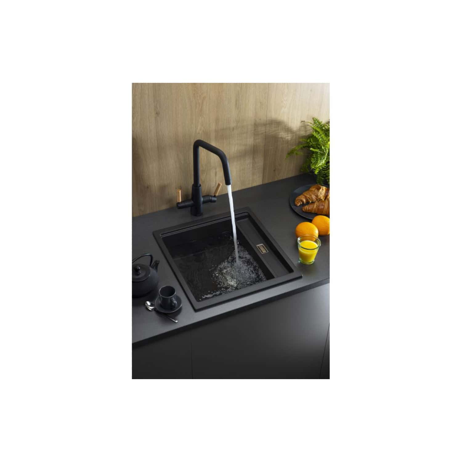 Drain-inset black kitchen sink with modern black faucet and running water, black countertop with fruit and herbs, contemporary design for Bubly Bathrooms in the UK.