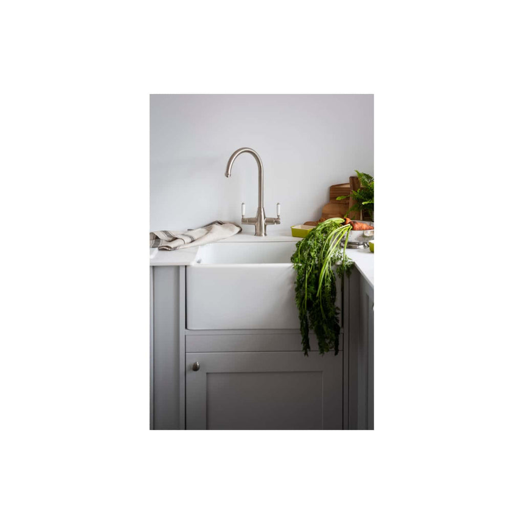 Shaker-style farmhouse kitchen sink with a contemporary stainless-steel faucet, surrounded by fresh vegetables, herbs, and natural wood accents in a modern, minimalistic kitchen setting.